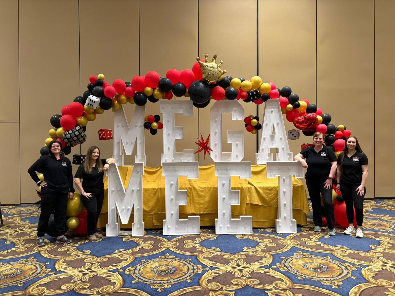 Meet staff standing beside the giant MEGA MEET marquee letters and balloon arch